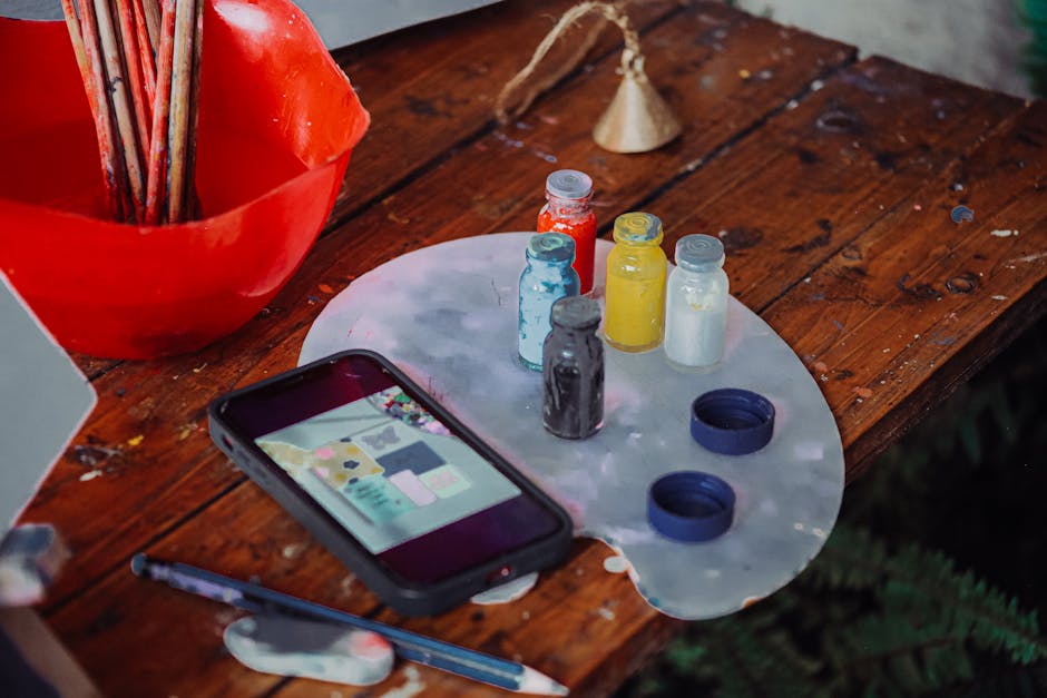 A vibrant artist's workspace with paint bottles, smartphone, and palette on a wooden table in Addis Ababa.