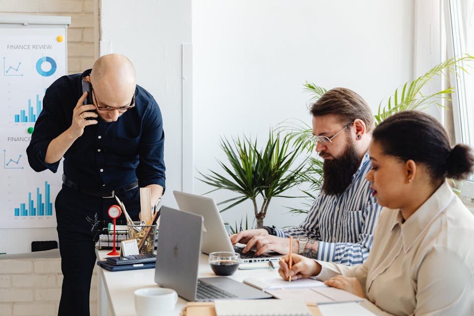 Office team engaged in collaborative tasks using laptops and phone in a modern workspace.